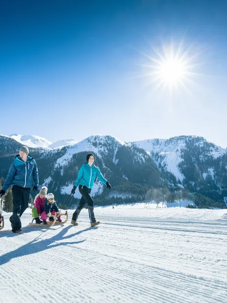 Rodeln Obertauern Familie wandert mit Schlitten im sonnigen Winterurlaub in den verschneiten Alpen